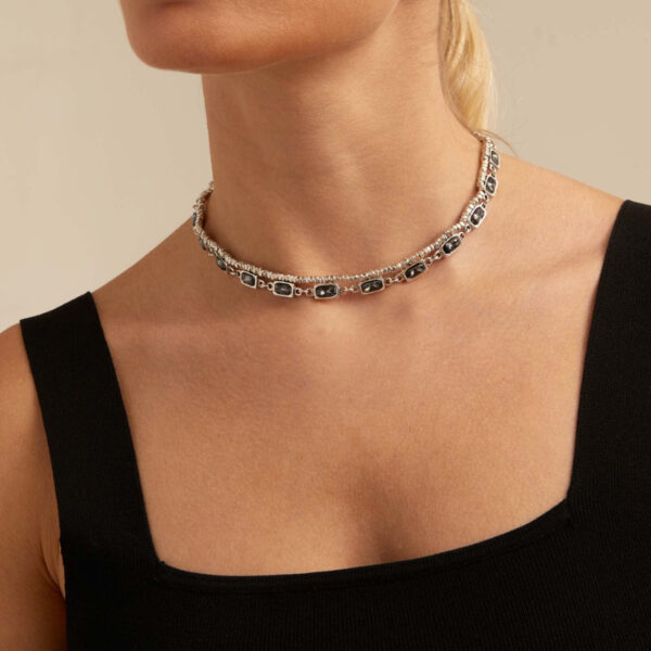 Short necklace featuring a strand of small cube seeds and 22 bevel settings with gray crystals. It features a lobster clasp, allowing you to adjust the necklace to the desired length. This necklace was handmade in Spain using a silver-plated metal alloy.